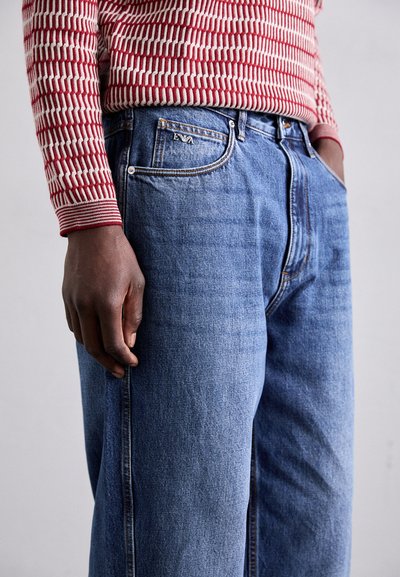 Lichtblauwe denim jeans met een relaxte pasvorm, met een klassiek vijf-pocket ontwerp en subtiele stikdetails. Getextureerde rode en witte gebreide trui.