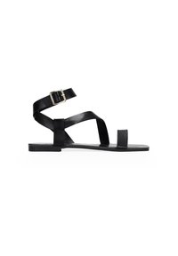 Sandal in pelle nera flat con cinturino alla caviglia, cinturini incrociati sopra il piede e design minimalista. Presenta una punta quadrata e una suola rettangolare.
