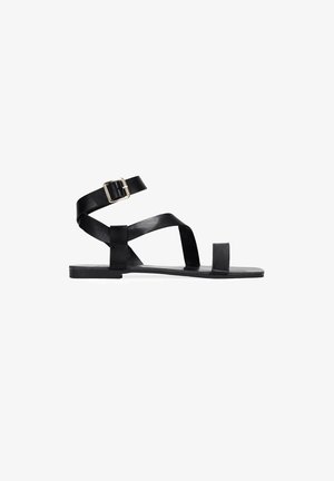 Sandal plana de cuero negro con una tira en el tobillo, tiras cruzadas sobre el pie y un diseño minimalista. Presenta una punta cuadrada y una suela rectangular.