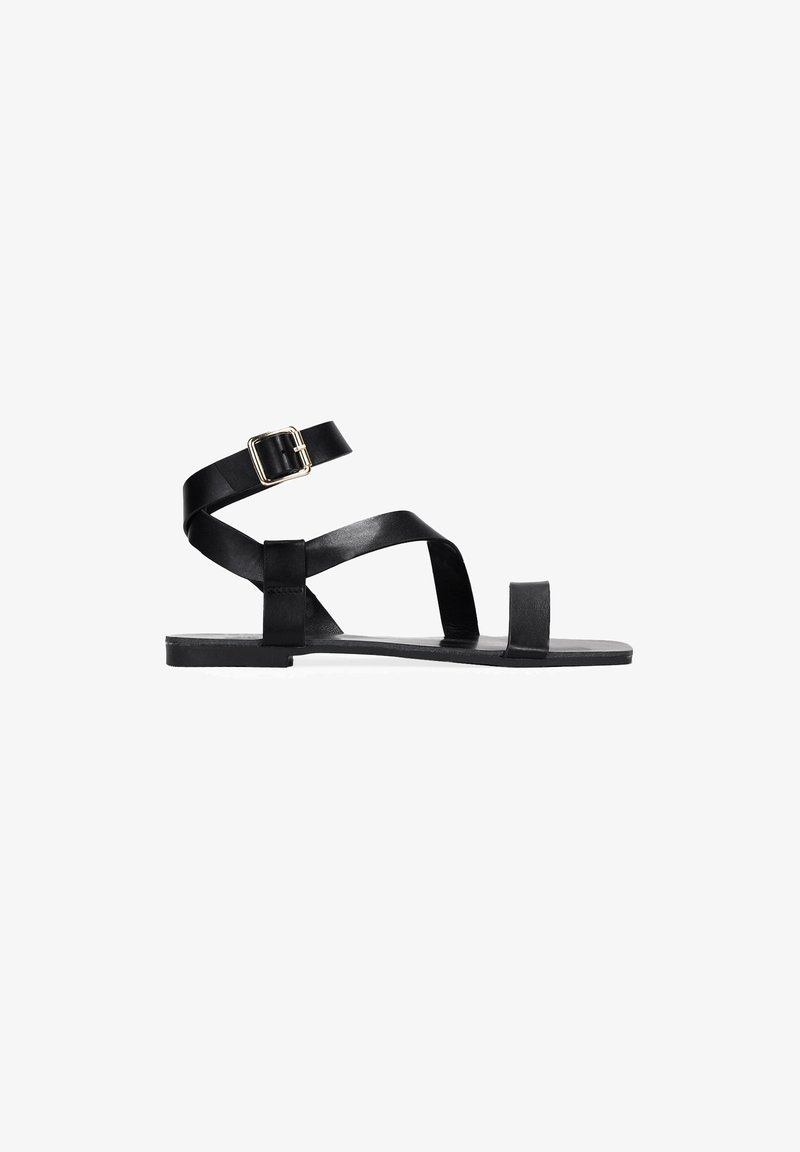 Sandal in pelle nera flat con cinturino alla caviglia, cinturini incrociati sopra il piede e design minimalista. Presenta una punta quadrata e una suola rettangolare.