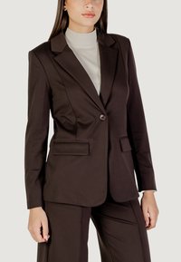 Blazer marrón a medida con solapas en pico, cierre de un solo botón y dos bolsillos frontales. Tejido suave, forma ajustada y diseño estructurado.