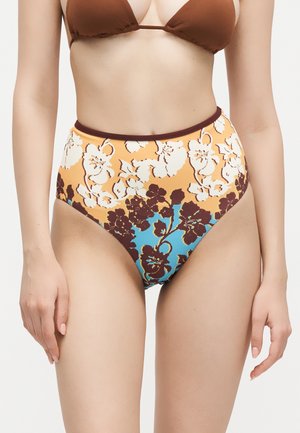 Kobieta nosząca bikini z wysokim stanem w żółto-niebiesko-brązowy wzór w kwiaty oraz brązowy top bikini.