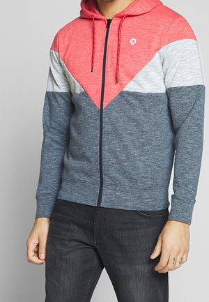 Sudadera con capucha y cremallera que presenta un diseño de bloques de color en rojo, gris y azul marino, confeccionada en un material suave con un acabado texturizado.