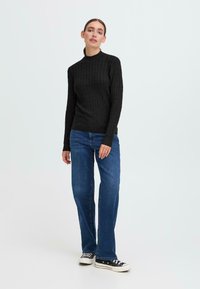 Schwarzer gerippter Strickpullover mit Rollkragen, kombiniert mit blauen geraden Jeans und schwarzen niederen Sneakers mit weißen Sohlen. Schlichtes und lässiges Design.