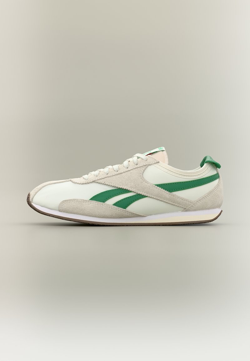 Λευκό sneaker χαμηλού προφίλ με πράσινες ρίγες και πάνελ από σουέντ, λευκά κορδόνια και καφέ λαστιχένια σόλα σε ουδέτερο φόντο.