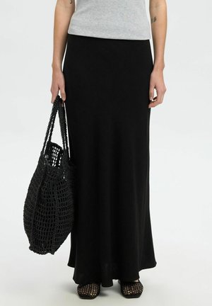 Gonna maxi nera in un tessuto morbido e fluido, abbinata a una borsa in tessuto nero intrecciato e scarpe col tacco aperto in mesh. Design e silhouette semplici.