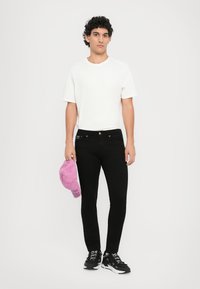 Melni džinsi ar zeltainiem aksesuāriem, vienkārša balta T-kreklu un roka turēts rozā cepures. Melni sporta apavi ar baltiem akcentiem. Minimalistisks dizains.