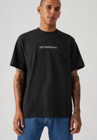 Svart bomull T-skjorte med teksten "LEVI STRAUSS & CO." i hvitt. Kortermet, avslappet passform, glatt tekstur og rund hals.