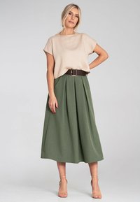 Beżowa bluzka z krótkim rękawem zestawiona z długą, zieloną spódnicą plisowaną, przewiązaną w talii szerokim brązowym paskiem. Prosty krój i lekka tekstura.