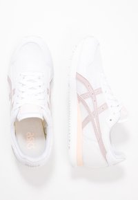 Vita atletiska skor gjorda av mesh och syntetiska material, med ljusrosa detaljer och en strukturerad sula med varumärke på tungan.