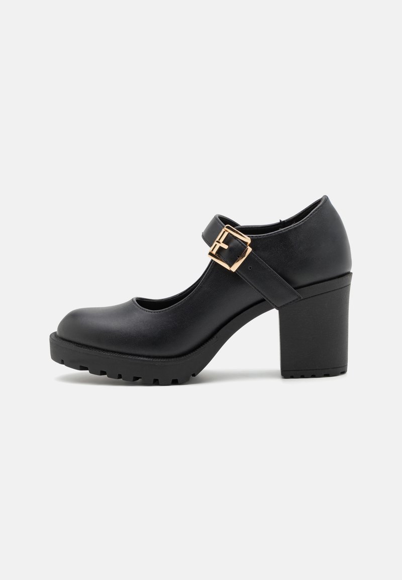 Chaussure Mary Jane noire avec talon haut épais, semelle crantée et bride à boucle dorée sur le cou-de-pied, vue de profil latéral.