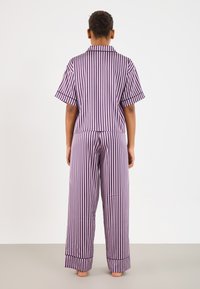 Fialovo-biele pruhované pyžamo so s krátkym rukávom a širokými nohavicami. Obsahuje golier a kontrastné manžety na rukávoch a nohaviciach.