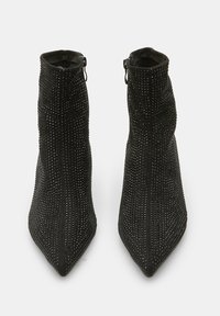 Botas de tobillo negras con diseño de punta afilada, cubiertas de pequeños rhinestones. Cuentan con un cierre de cremallera en el lateral. Textura similar al ante.