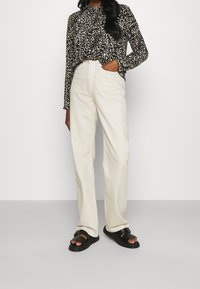 Camicia a maniche lunghe a righe bianche e nere, pantaloni crema a vita alta e sandali neri, con vestibilità rilassata e texture morbide.