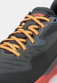 Chaussure de sport noire avec une tige texturée, dotée de lacets et d'accents orange. Comprend des superpositions synthétiques et un design de semelle robuste.