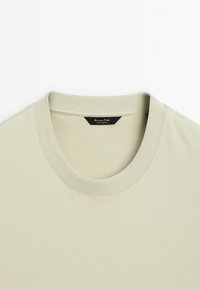 T-shirt beige en coton à col rond avec col côtelé et étiquette de marque noire cousue à l'intérieur de l'encolure.