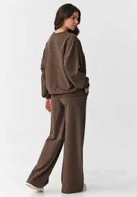 Brązowa, oversize'owa bluza oraz pasujące szerokie spodnie wykonane z miękkiego materiału. Ubranie charakteryzuje się luźnym krojem i prążkowanymi mankietami.
