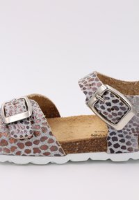 Sandale ouverte avec un motif à pois argenté et marron, semelle en liège, boucle métallique ajustable et semelle en caoutchouc blanche.