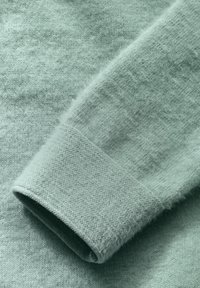 Mjukt, ljusgrönt stickat tyg med en slät textur, som har detaljer med viken ärm och subtila färgvariationer.