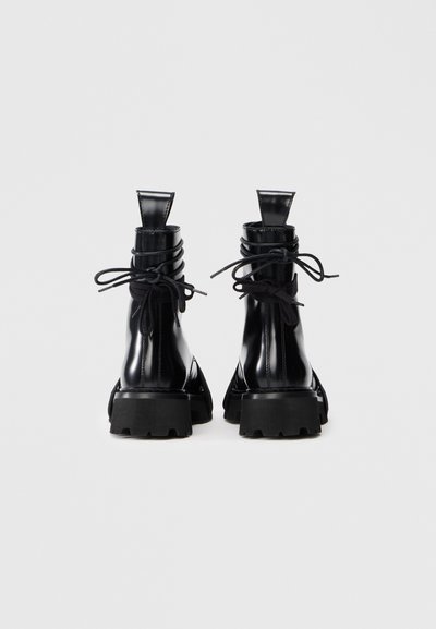 Stivali neri alla caviglia con finitura lucida, punta rotonda, suole spesse in gomma nera e design con lacci sul retro. Stile minimalista e costruzione robusta.