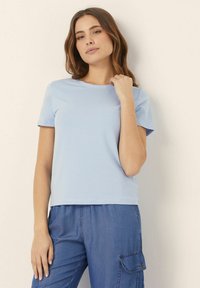 Tricou scurt cu mâneci scurte, de culoare albastru deschis, dintr-un material de bumbac moale, având un decolteu rotund și o croială lejeră. Purtați-l cu pantaloni cargo din denim.