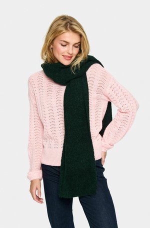 Scarf in lana verde scuro adagiato su un maglione rosa chiaro lavorato a maglia con un motivo in pizzo, abbinato a jeans blu scuro.