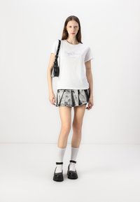 Vit bomull t-shirt med logotyp, grå plisserad minikjol, svart väska, svarta skor med spännen och vita strumpor. Enkel design, avslappnad stil.