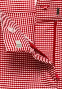 Rood en wit geruite stof heeft een pocket met een rode rits, duidelijke knoophardware en contrasterende stikdetails.