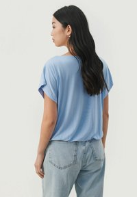 Lyseblå kortærmet top lavet af blødt stof, indeholdende en løs pasform og rund halsudskæring, parret med lyseblå jeans.