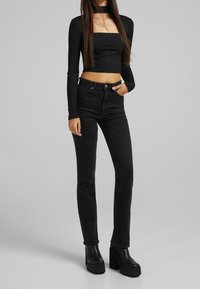 Top corto negro de manga larga con cuello cuadrado, combinado con unos jeans negros de cintura alta y botas de plataforma negras y gruesas.