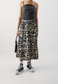 Denim top med sølvnitter og tynde stropper, parret med en mønstret midi-nederdel i sort og beige. Sorte sneakers og en lille sort taske fuldender looket.