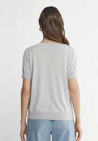 Hellgraues gestricktes Oberteil mit kurzen Ärmeln, lässiger Passform, Rundhalsausschnitt und geripptem Saum, kombiniert mit hellblauen Jeanshosen.