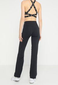 Schwarze sportliche Leggings aus dehnbarem Stoff, kombiniert mit einem schwarzen Sport-BH mit gekreuzten Trägern und Nike-Logo.