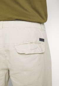 Ljusbeiga linbyxor har en bakficka med lock och en liten märkesetikett. Midjan är elastisk för extra komfort.