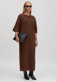 Braunes gestricktes Kleid mit kurzen Ärmeln, das bis zur Mitte der Wade reicht. Getragen mit schwarzen spitzen Stiefeletten und einer schwarzen Clutch.