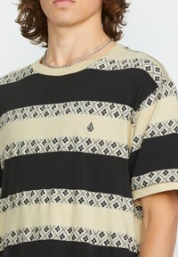 Kortærmet T-shirt med sorte og cremefarvede striber, samt et mønstrede vandret bånd. Tekstilet er blødt bomuld og inkluderer logo-detaljer.