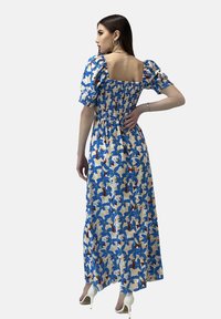 Maxikleid mit blauem Blumenmuster, Puffärmeln, gerafftem Oberteil und offenem Rückendetail. Der Stoff hat eine leichte Textur und ein fließendes Design.