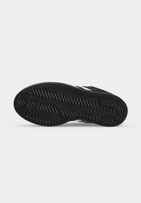 Schwarze Sneakersohle mit strukturiertem Zickzack- und geometrischem Profilmuster auf hellgrauem Hintergrund.