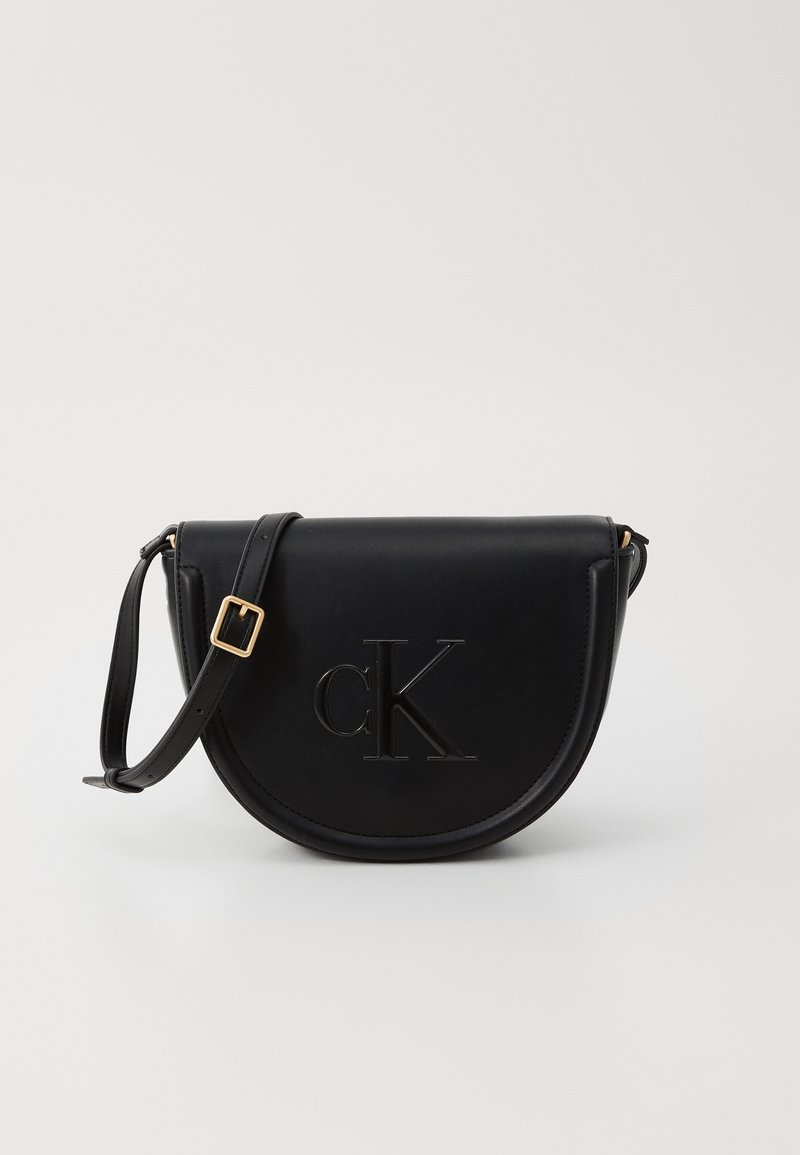 Black leather crossbody bag with a rounded, half-moon shape, embossed "cK" logo, gold-tone buckle hardware, and an adjustable strap.