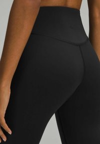 High-waisted black leggings made from stretchy, smooth fabric. Features a seamless design and minimal logo detailing on the waistband.