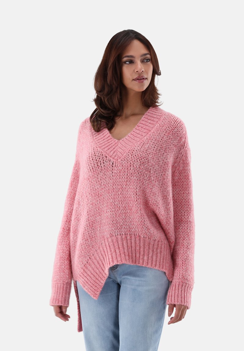 Lässiger, rosa V-Ausschnitt-Pullover mit strukturiertem Strick, langen Ärmeln und einem verlängerten Rücken, kombiniert mit hellblauen Jeans.