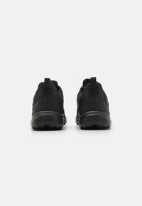 Black athletic shoes with a textured surface, featuring pull tabs at the heel and rugged rubber soles, designed for traction and stability.
