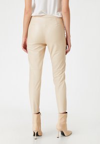 Beige faux læderbukser der sidder tæt om anklerne, med en tapered ben-design, en glat tekstur og uden synlige lommer, parret med højhælede støvler.