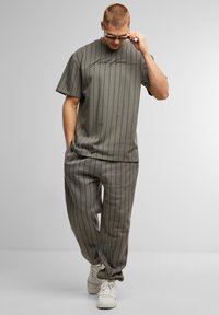 Camiseta gris rayada con cuello redondo y estampado en cursiva negro, combinada con pantalones a rayas grises a juego y zapatillas blancas.