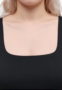 Gros plan d'une personne portant un haut noir avec un décolleté carré montrant le cou, les clavicules et le haut de la poitrine.