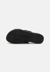 Black rubber shoe sole features a ribbed pattern, embossed logo reading "Calvin Klein Jeans," and a smooth, uniform shape.