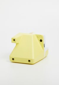 Yellow plastic instant camera with a triangular shape, white accents, a power button, and a colorful stripe on top. Glossy finish.