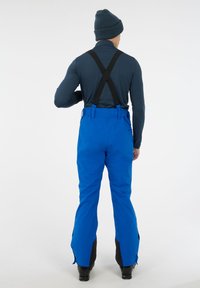 Blauwe waterdichte sneeuwbroek met zwarte verstelbare bretels, taps toelopende pijpen en zijritsen bij de enkels voor gebruiksgemak.