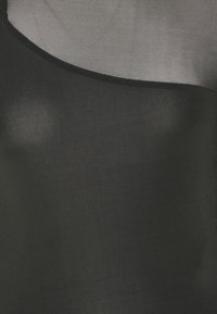 Genomskinlig svart tyg med ogenomskinlig svart panel över bröstet och en nätliknande genomskinlig överdel.