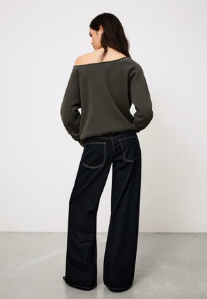 Hanorac gri închis cu umerii goi și ținte argintii la decolteu, combinat cu blugi din denim închis cu picioare largi, având buzunare în spate.